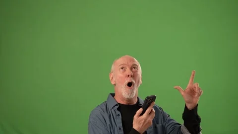 Senior Man Expressing Joy While Holding Smartphone Against a Green Screen Stock Footage 305522982