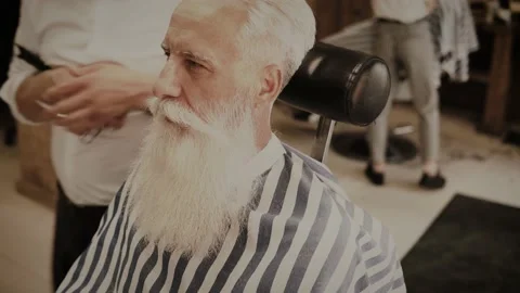 Senior man getting styling and trimming of his beard in the barbershop Stock Footage 233653460