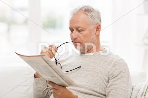 Senior man in glasses reading newspaper at home Stock Photos