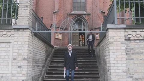 Senior man goes down steps near church while guy shots video Stock Footage 139795995