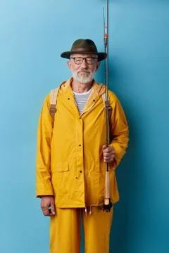 Senior man in green hat and yelow raincoat holding fishing rod Stock Photos