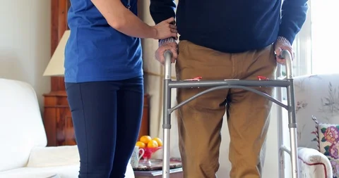 Senior Man With Hands On Walking Frame Being Helped By Care Worker Stock Footage 119953027