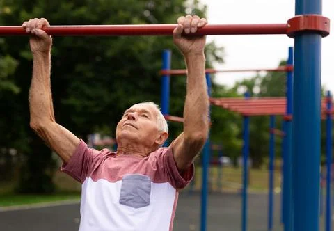 Senior man hanging from pullup bar outoors Stock Photos