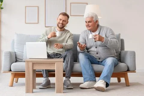 Senior man with his son drinking coffee while watching something on laptop at Stock Photos