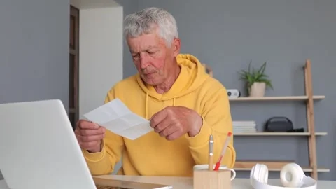 Senior man holding documents and using laptop at home checking bills taking Vídeos de archivo 292761297