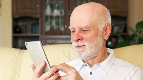 Senior man at home using cellphone, browsing, reading news. Active modern life Video stock 86489513
