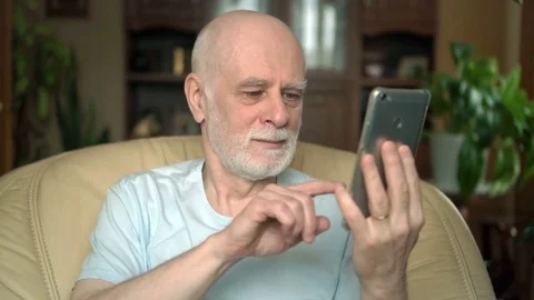 Senior man  at home using smartphone, talking with friend via messenger app Video stock 74638872