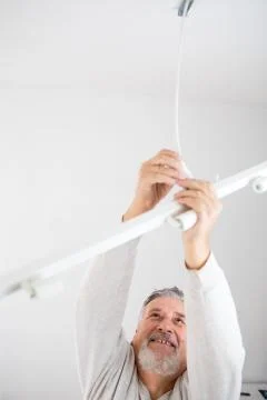 Senior man installing a ceiling light n a freshly renovated appartment Fotos Stock