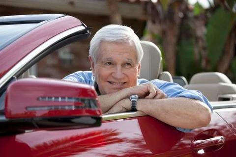 A senior man leaning on the door of his convertible sports car Stock Photos