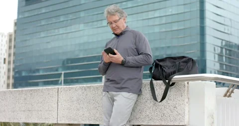 Senior man leaning on railing at walkway, scrolling phone to check emails, Stock Footage 345062673