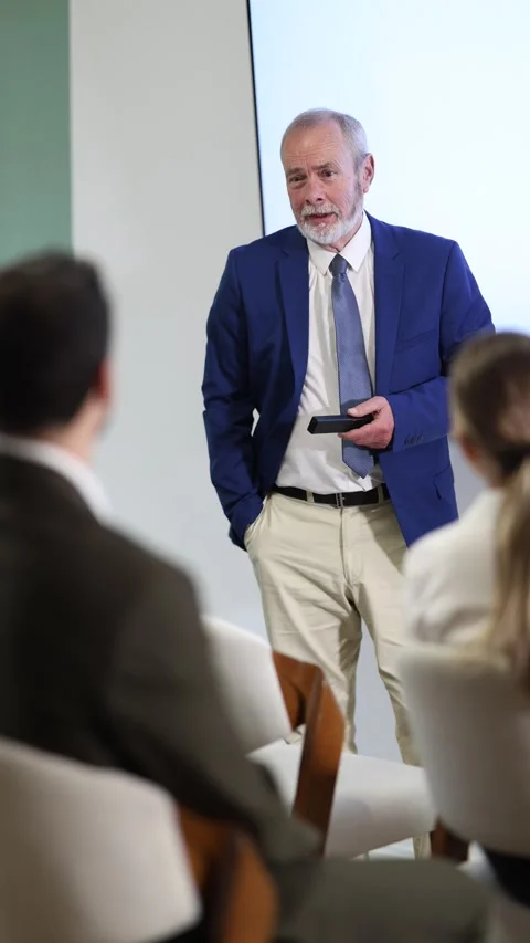 Senior man lecturer with remote controller speaks to business audience of Stock Footage 332641264