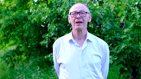 Senior man looking at camera while finishing a tasty bite of food near apple Stock Footage 345336082