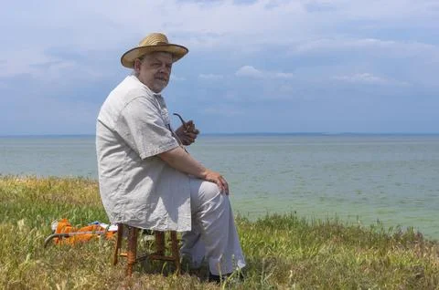 Senior man looking into the distance while sitting on wicker small stool Stock Photos
