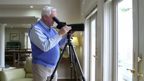 Senior man looking through patio door with a telescope Stock Footage 83394439