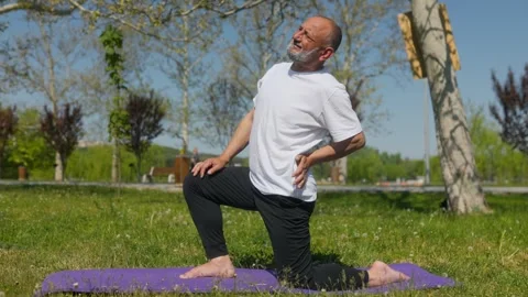Senior man with lower back pain during fitness workout on mat in park Vidéo 334869066