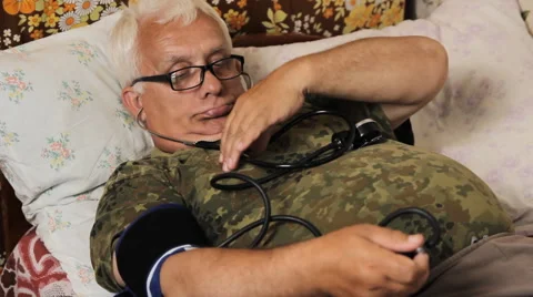 Senior man lying on the bed and measures the blood pressure itself Stock Footage 64770570