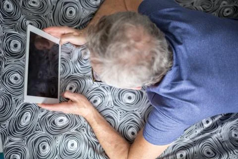 Senior man lying on bed using tablet Stock Photos
