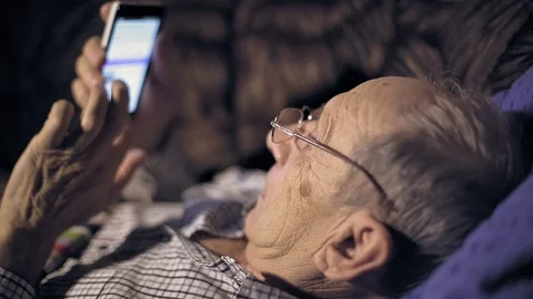 Senior man lying with smartphone on the couch and watching the news, the screen  Stock Footage
