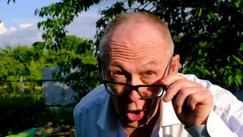Senior man making funny faces and peeking over glasses at camera near apple Stock Footage 345334692