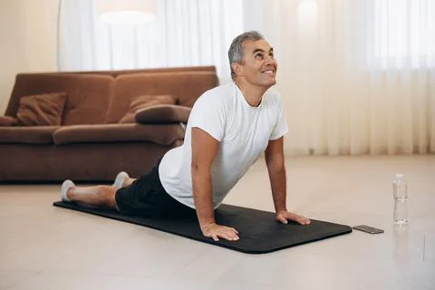 Senior man meditating while doing cobra pose in living room. Stretching Stock Photos