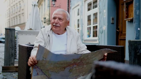Senior man with mustache holds map sitting in street cafe Stock Footage 115884366