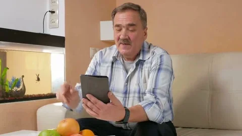 A senior man with a mustache talking on a tablet computer with relatives. He Stock Footage 69212127