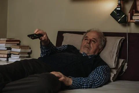 Senior man napping while lying down in bed and watching TV with a television Stock Photos