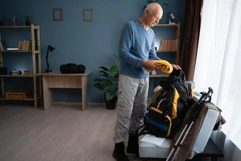 Senior man packing his backpack to hiking trip at home. Travel and hike Stock Photos