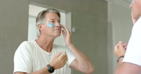 Senior man peeling blue hydrogel eye patches under eyes at bathroom mirror, Stock Footage 340257373