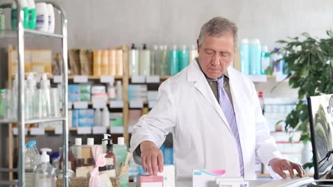 Senior man is a pharmacist typing on a computer, bringing in new goods and Vídeos de archivo 335614971