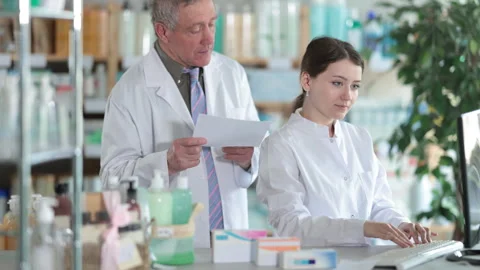 Senior man pharmacist use computer, girl intern with prescription Stock Footage 310686421