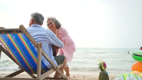Senior man playing guitar while sitting on a beach chair Stock Footage 338388541