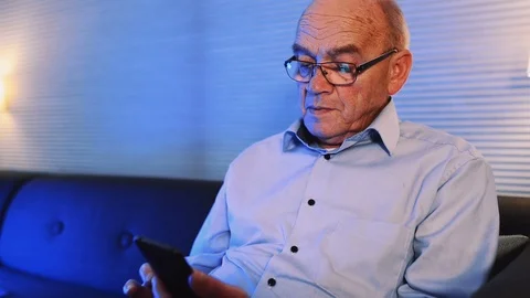 Senior man plays with mobile phone and types on it while sitting at home Stock Footage 99014875
