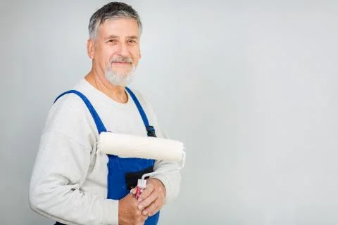 Senior man posing with a paint roller after having paint a white wall Fotos de archivo