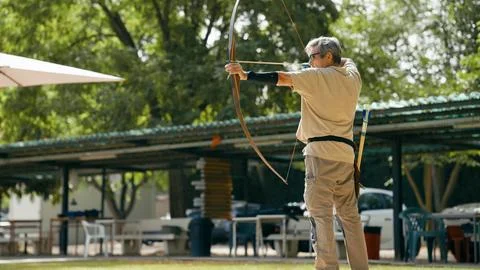 Senior man practicing archery, aiming at goals Stock Photos