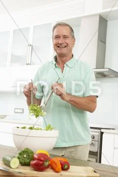 Senior Man Preparing Salad In Modern Kitchen Stock-Fotos