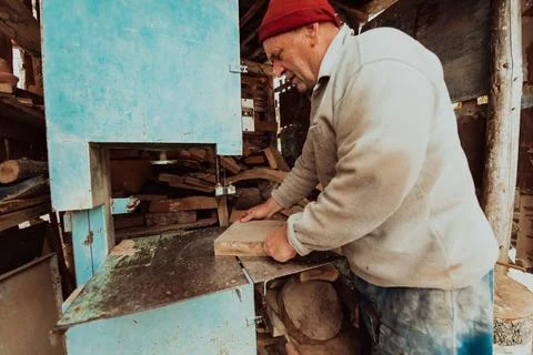 A senior man processing wood on a machine in an outdoor workshop. Stock Photos