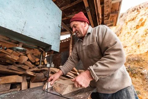 A senior man processing wood on a machine in an outdoor workshop. Stock-Fotos