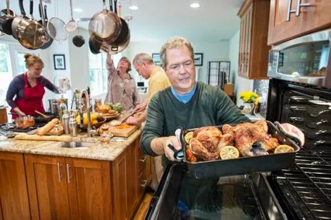 Senior man pull roast chickens out of the oven at a home dinner party. Stock Photos