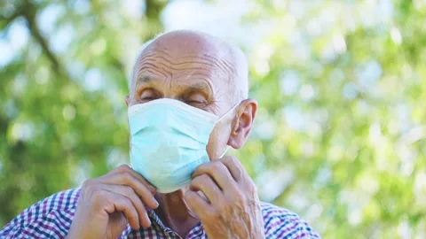 Senior man puts on blue mask hiding smile against garden Video stock 163242559