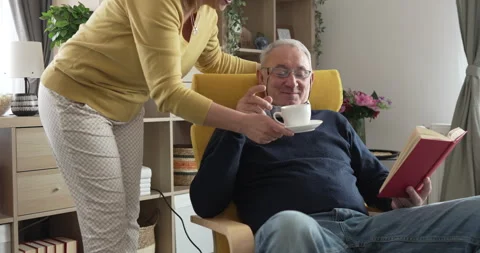 Senior man read book while his wife bring him cup of coffee at home Stock Footage 271157200