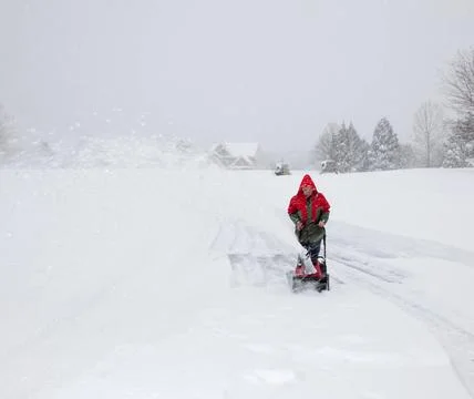 Senior man in red coat using a snow blower during a blizzard on home drive... Stock Photos