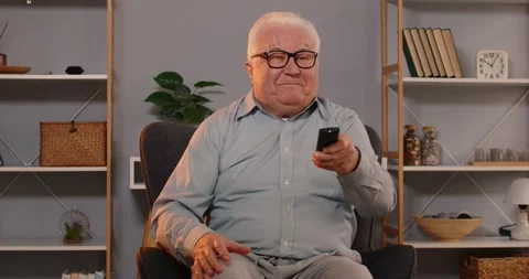 Senior man with remote controller sitting at home and switching channels Video stock 295133179