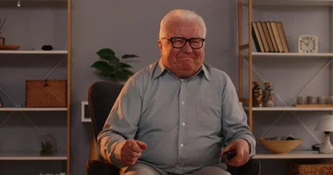 Senior man with remote controller sitting at home and switching channels Video stock 307919951