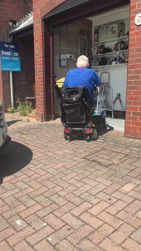 Senior man riding mobility scooter out of residential garage in Poole Dorset Stock Footage 340597579