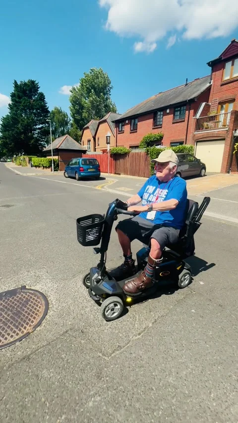 Senior man riding mobility scooter across residential street in Poole Dorset Stock Footage 340597730