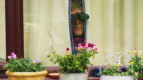 A senior man in a room using a pair of binoculars through curtains. Video stock 246629684