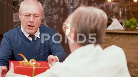 Senior man shocked by the gift that his wife gave him during mealtime in a Stock Photos