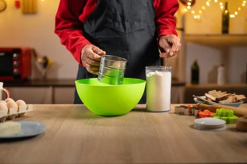 Senior man sifting flour while preparing Christmas cookies dough Stock Photos