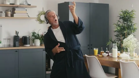 Senior man singing and playing at fake guitar at morning in the kitchen Stock Footage 218717403